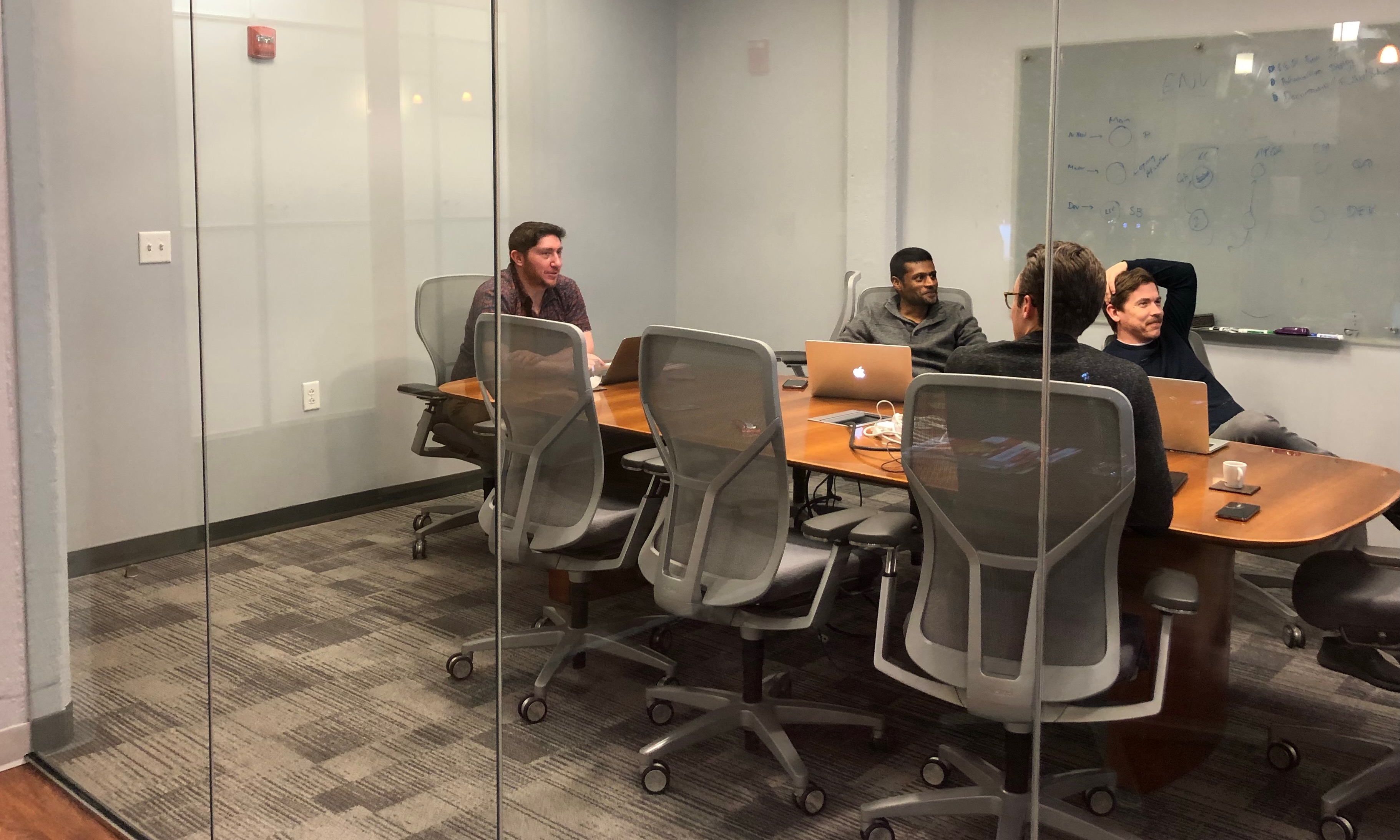 Photo of team meeting in a conference room, taken from the outside looking in through a glass wall.